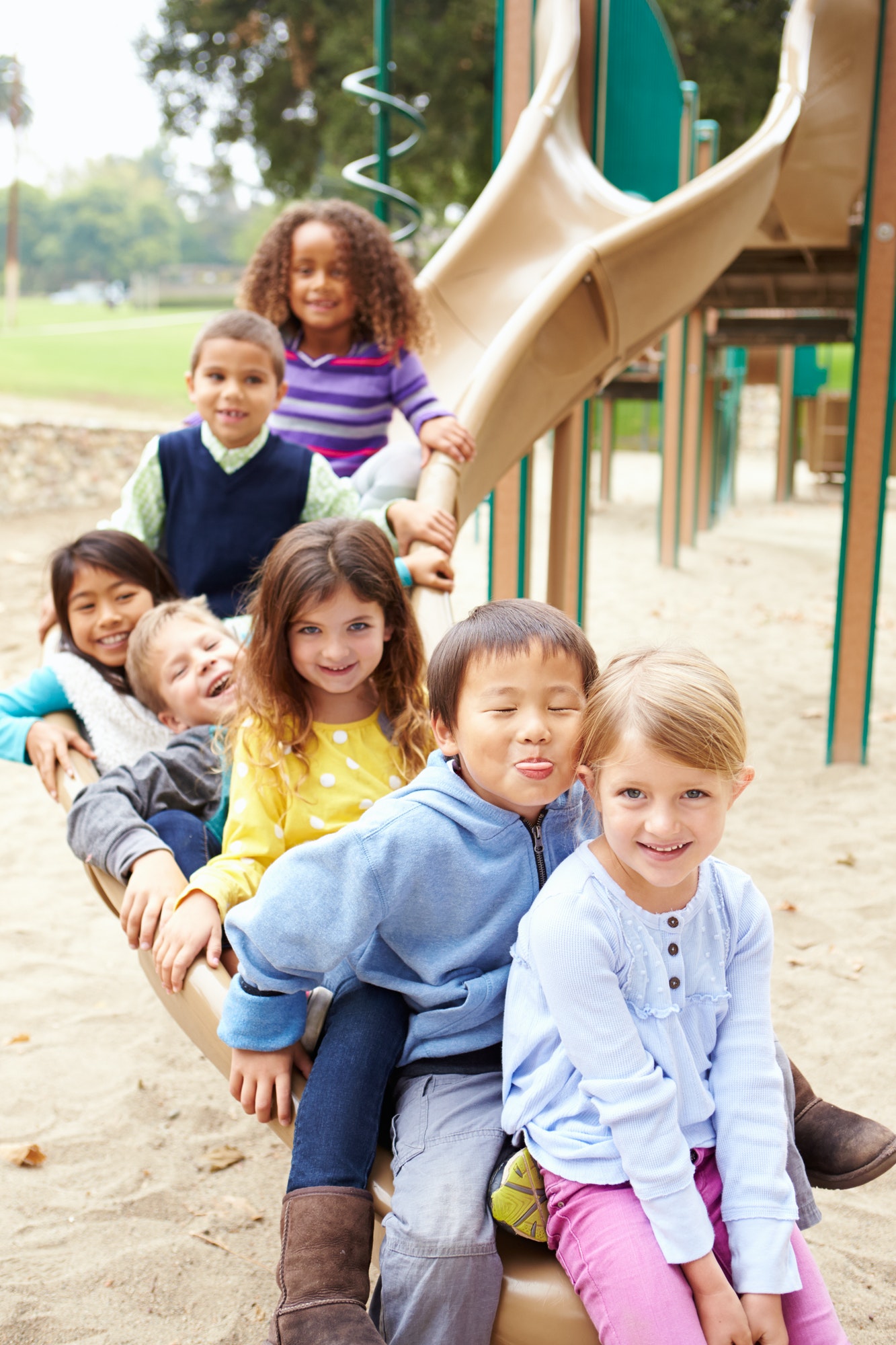 Group Of Young Children Sitting On Slide In Playground