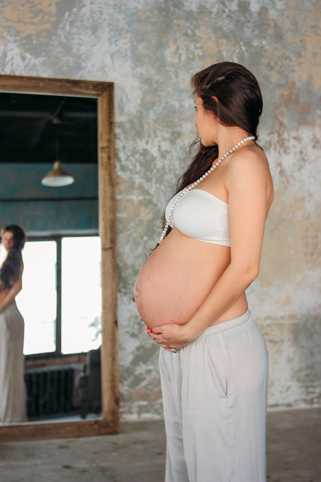 Tall beautiful pregnant girl young woman with long curly hair standing in front of the mirror in